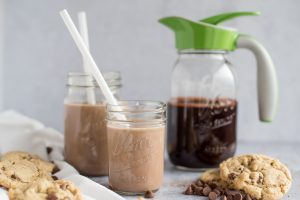 Mason jar with chocolate syrup and an Ergo Spout with two glasses of chocolate milk on the side - side view