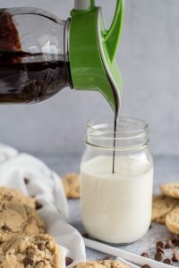 Ergo Spout pouring chocolate syrup from a mason jar into a glass of milk - Side view