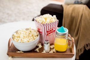 TV tray by sofa with bowl of popcorn and melted butter in mason jar with Ergo Spout Mini on top