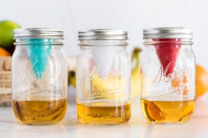 3 mason jars, each with a fruit fly funnel. One red, one white and one teal